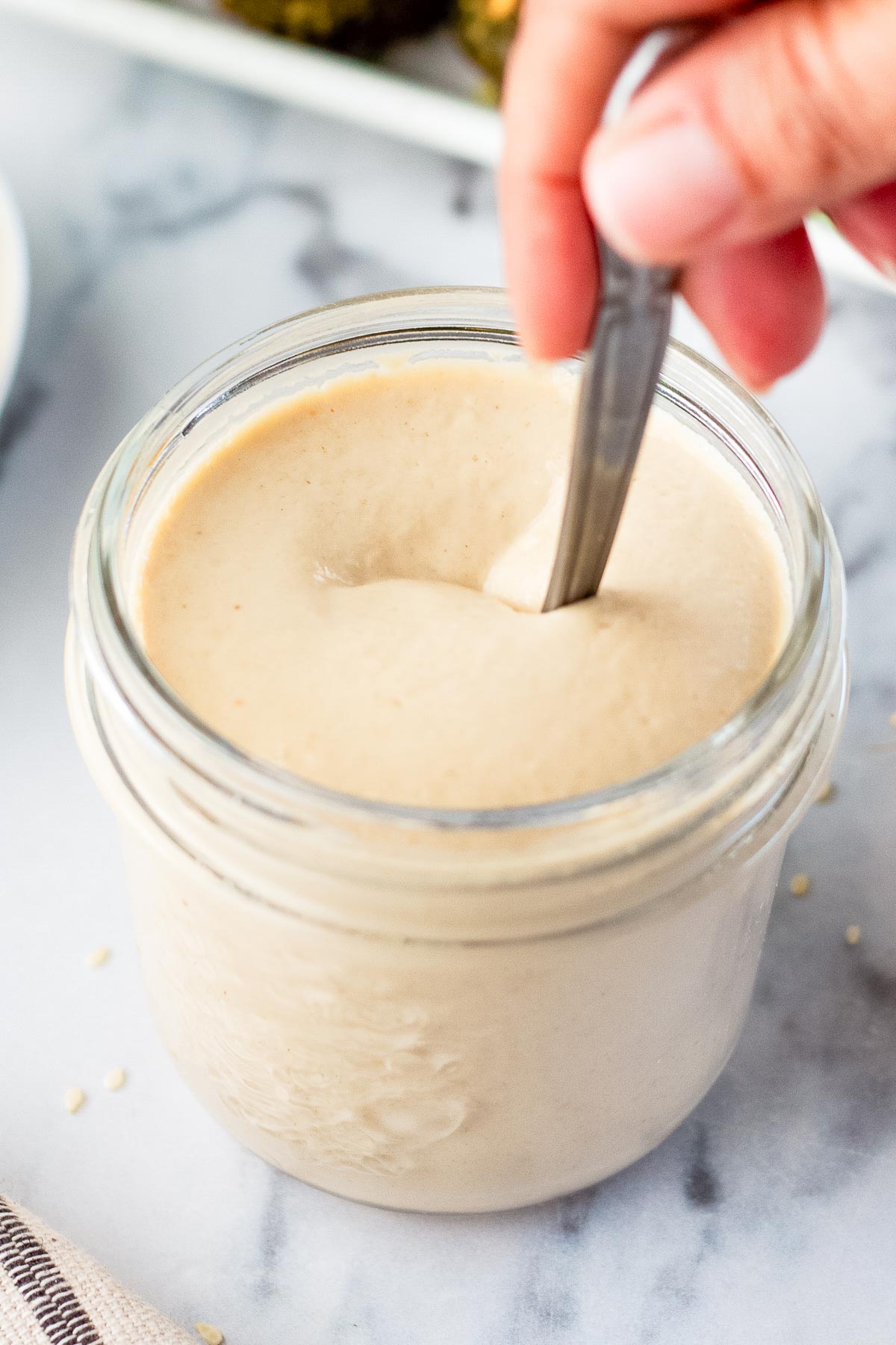 hand mixing tahini sauce in a glass jar.