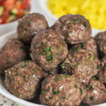 beef kofta kebabs in a white bowl with rice and israeli salad in the background.