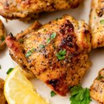 close up photo of baked lemon pepper chicken thighs on a plate with lemon wedges and parsley garnish.