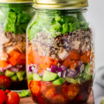 salad in a jar layered with chicken, lettuce, quinoa, bell pepper, red onion, cucumber, tomato and dressing.