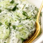 creamy cucumber salad in a bowl with a gold fork.