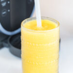 pineapple orange juice slushi in a glass with a straw with ninja sushi behind it.