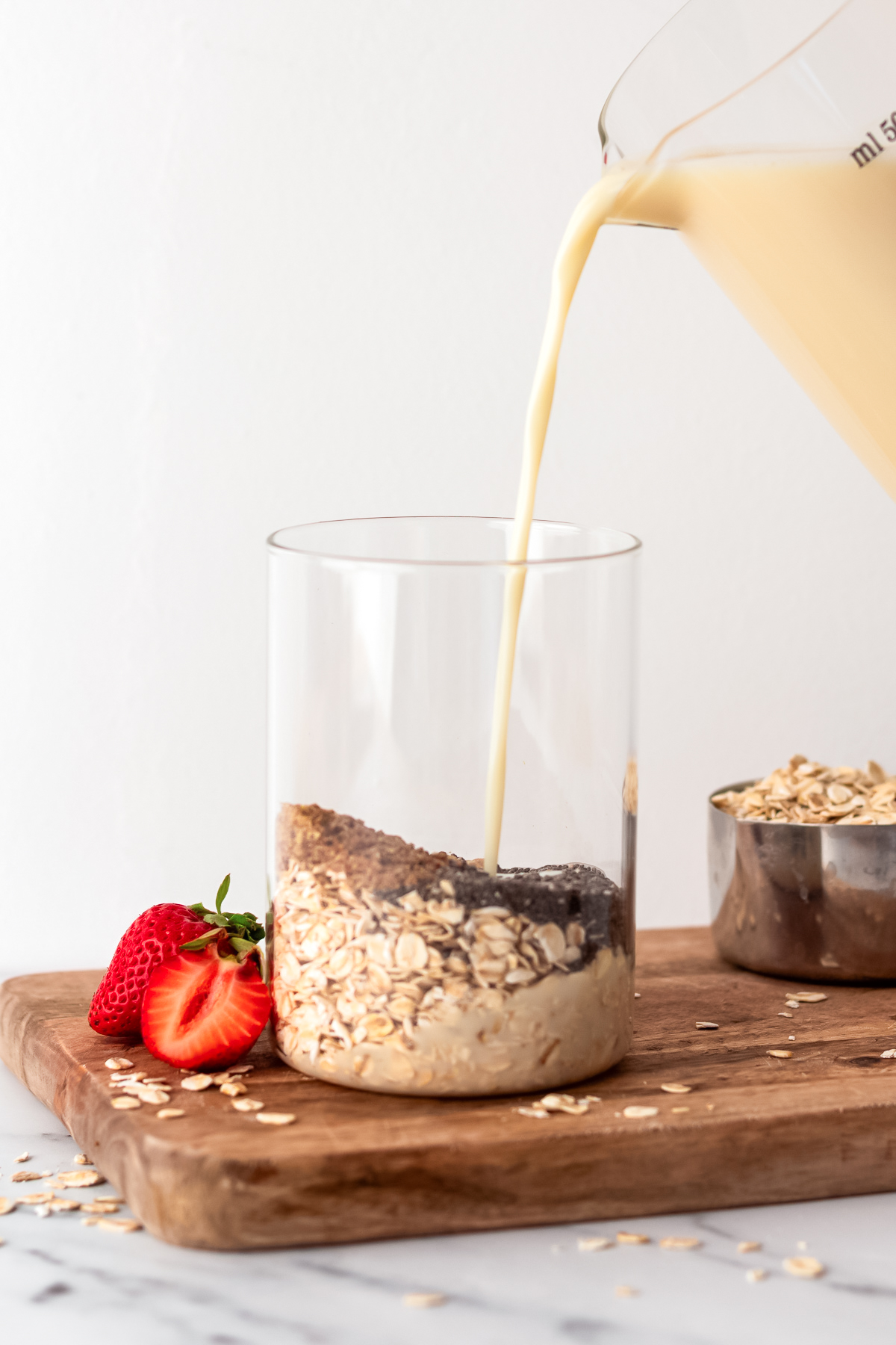 dairy free milk pouring into glass jar of overnight oats ingredients.