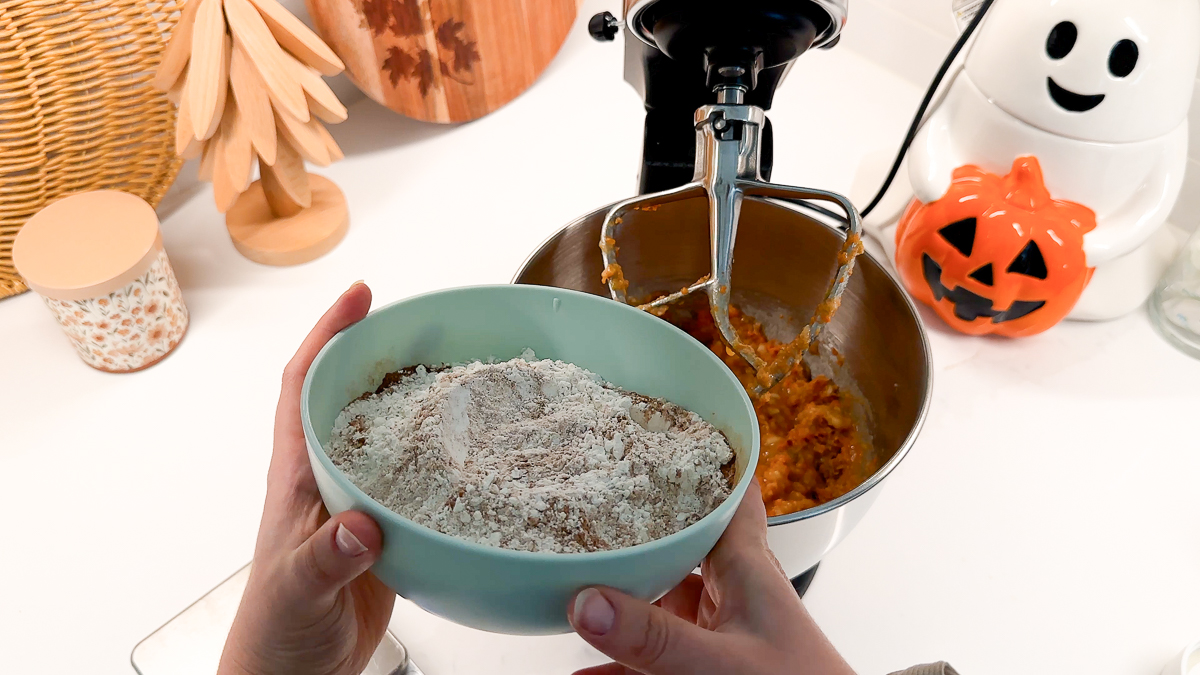 hand holding dry ingredient bowl above mixer.