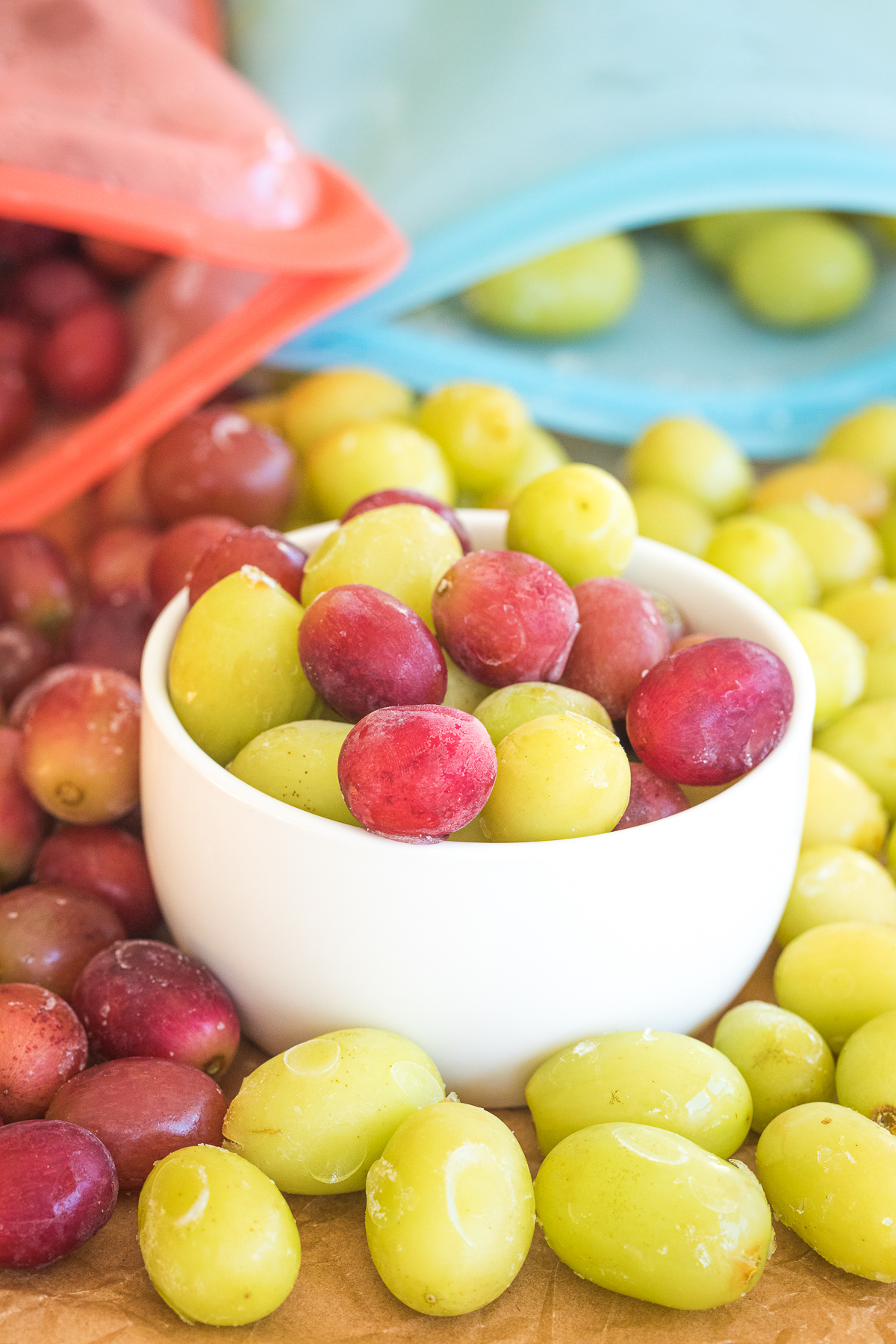 frozen grapes in a bowl with stasher bags with frozen grapes behind it.
