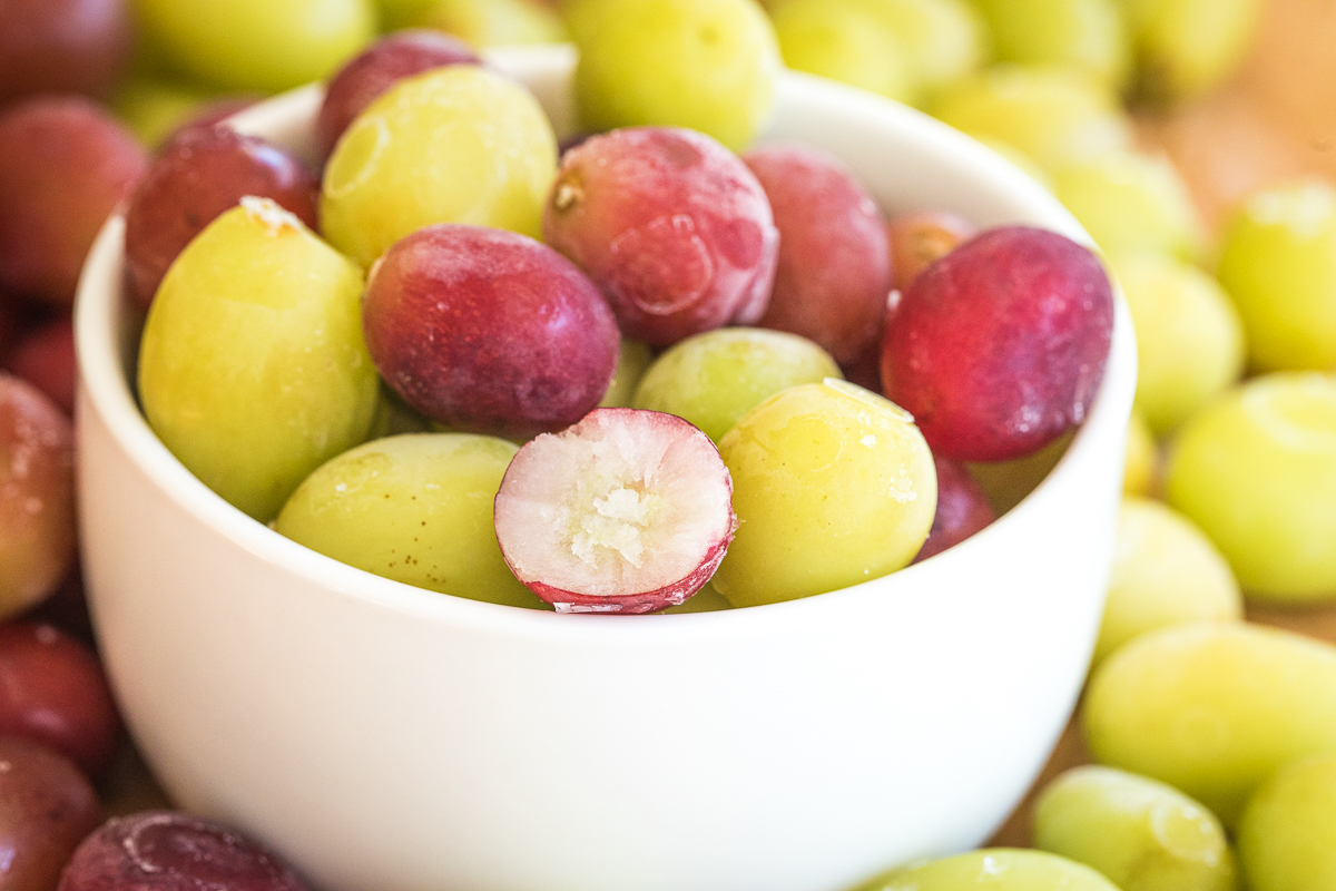 frozen grapes in a bowl, with one cut in half showing the inside frozen.