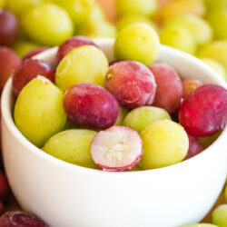frozen grapes in a bowl, with one showing the inside frozen.