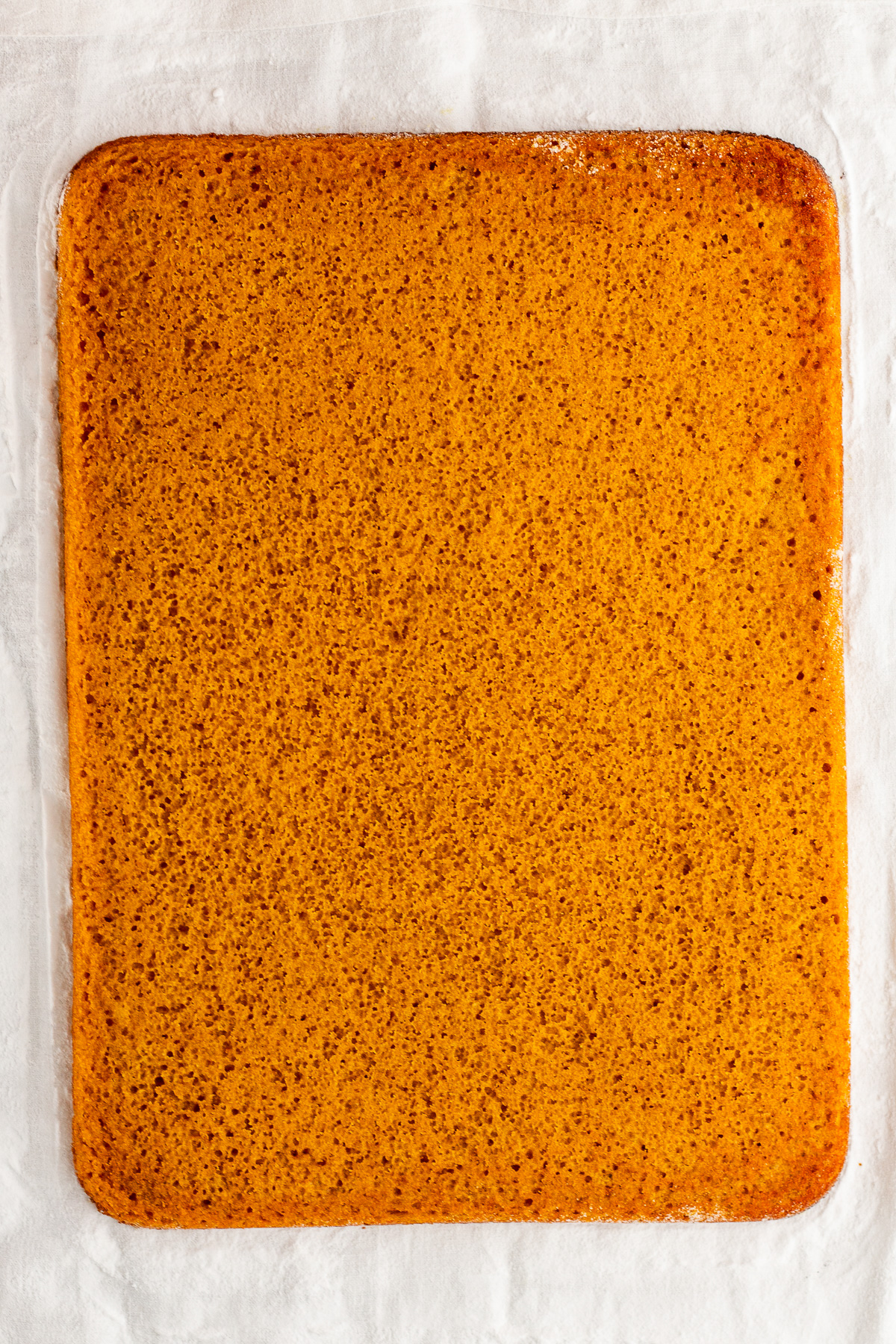 baked pumpkin roll cake on powdered sugar lined towel.