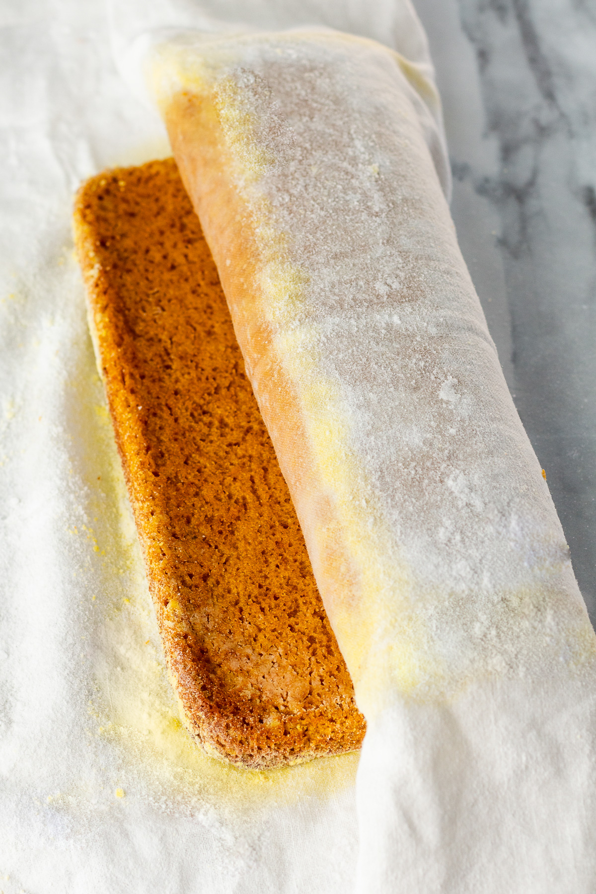 partially rolled pumpkin roll cake in powdered sugar rolled towel.