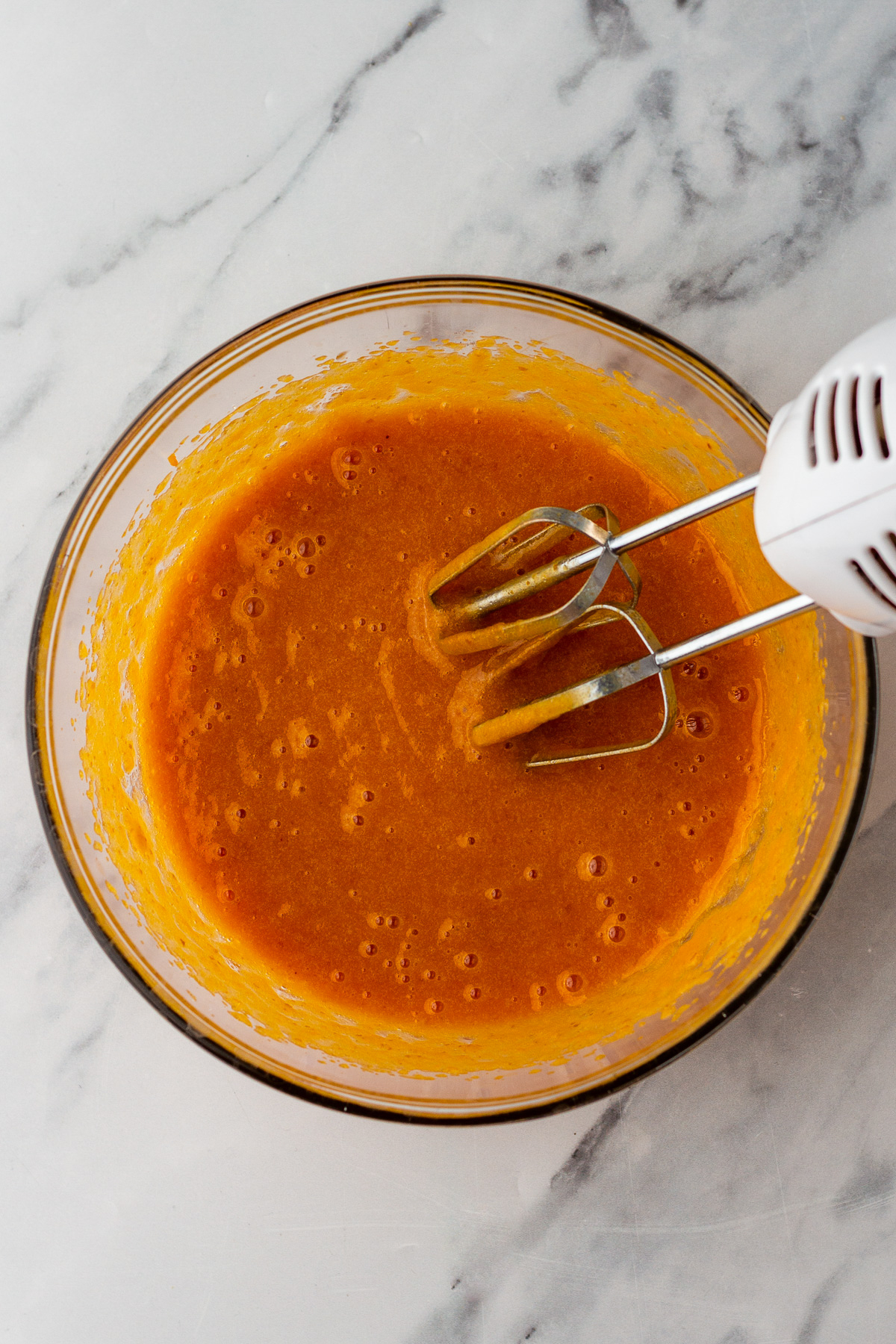 ingredients for pumpkin roll cake in a bowl with hand mixer mixed.
