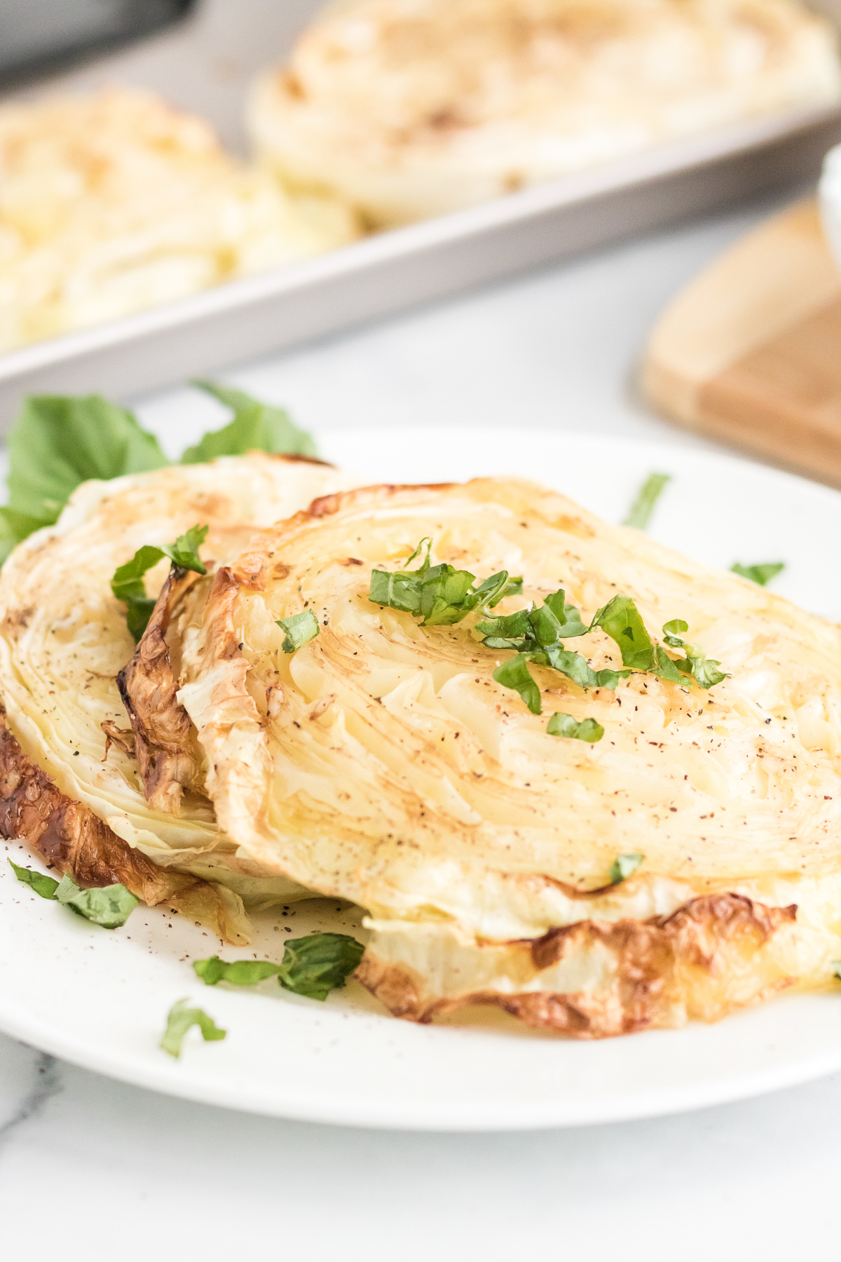 Close-up of roasted cabbage steaks garnished with chopped fresh herbs on a white plate.