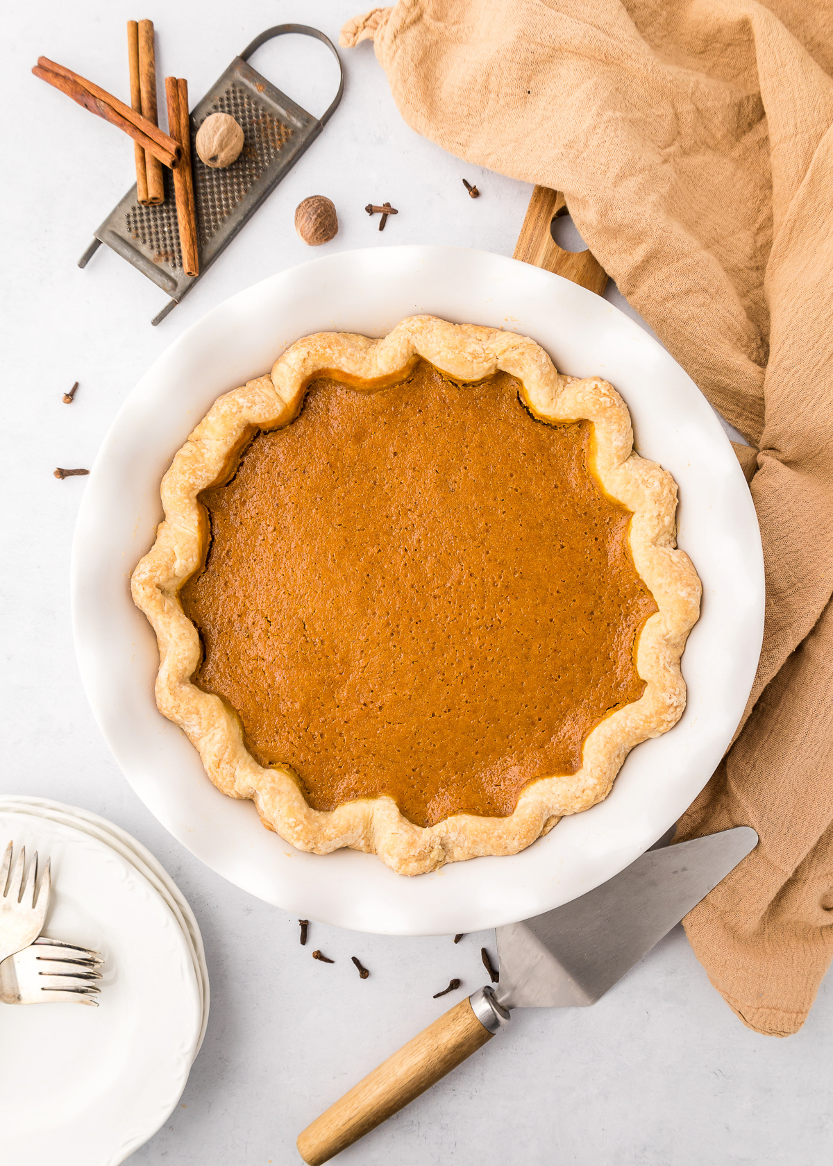 Overhead view of a whole pumpkin pie in a white dish surrounded by forks and fall spices.