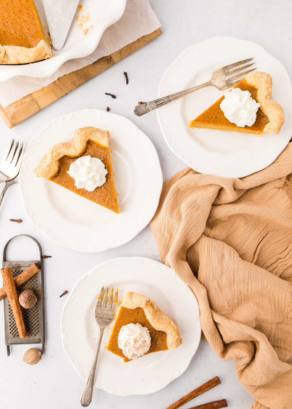 Overhead view of three slices of pumpkin pie on white plates topped with whipped cream.
