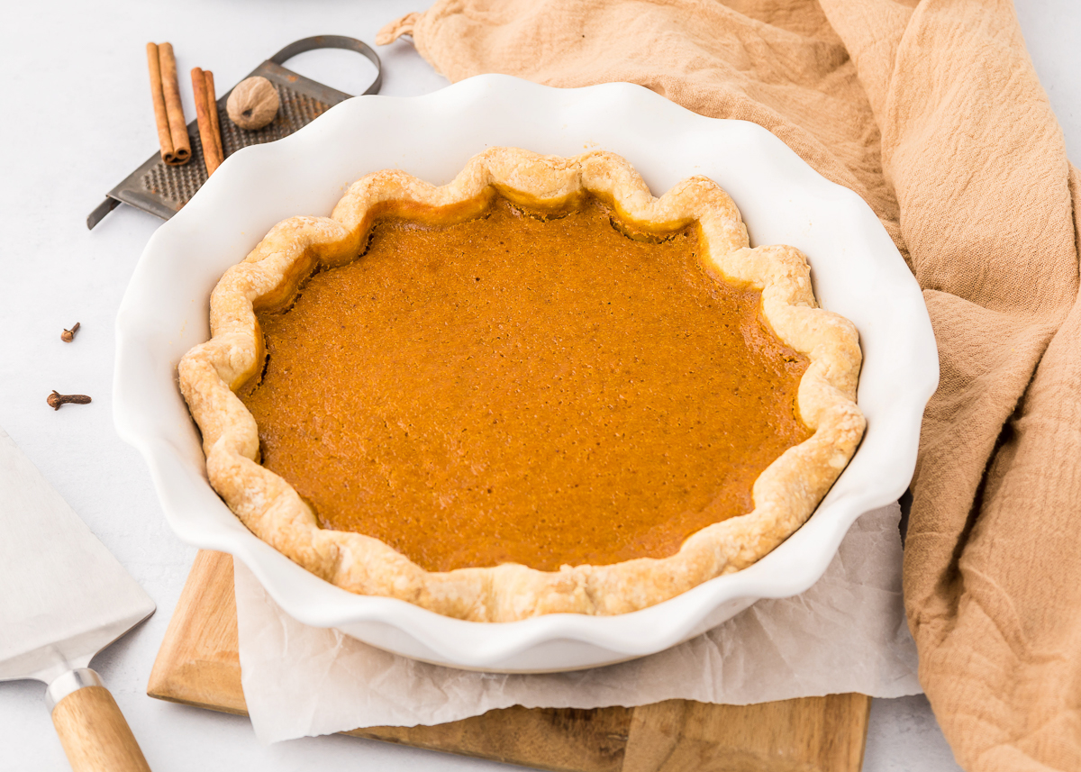 Baked pumpkin pie in a white ceramic pie dish with flaky crust and warm fall spices.